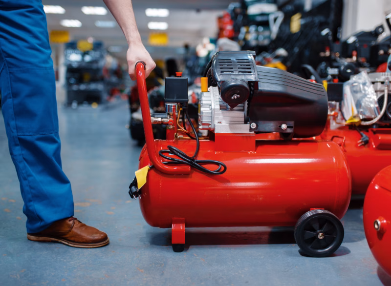 Customer examining a portable red air compressor with a black motor in a hardware store aisle