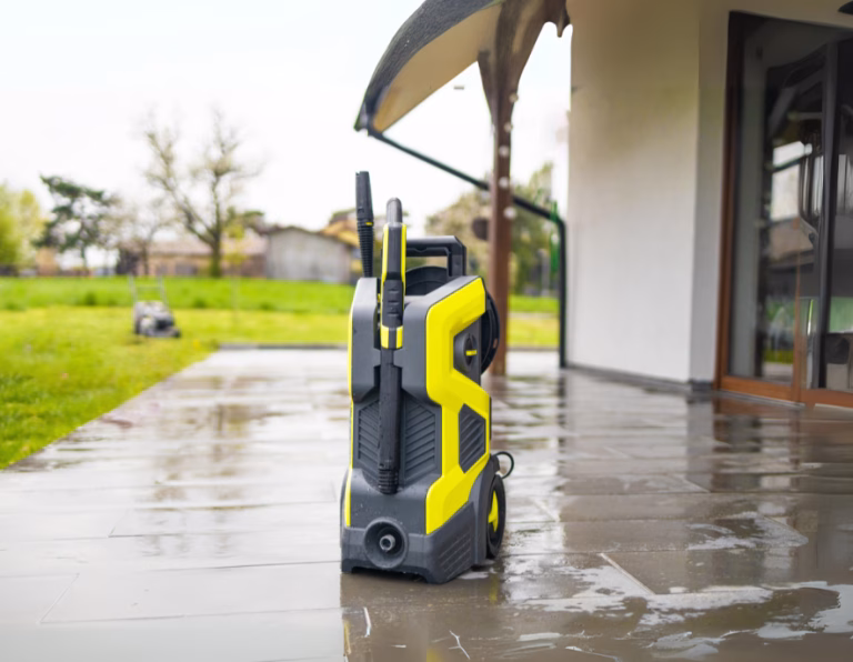 Yellow and black electric pressure washer on a wet patio outside a modern house
